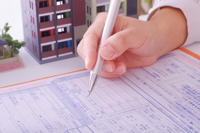 契約書にサインをする人の手元とマンションの模型